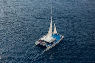 Vista aérea de um catamarã navegando com passageiros em águas azuis