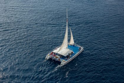 Vista aérea de um catamarã navegando com passageiros em águas azuis