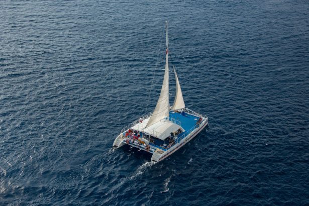 Vista aérea de um catamarã navegando com passageiros em águas azuis