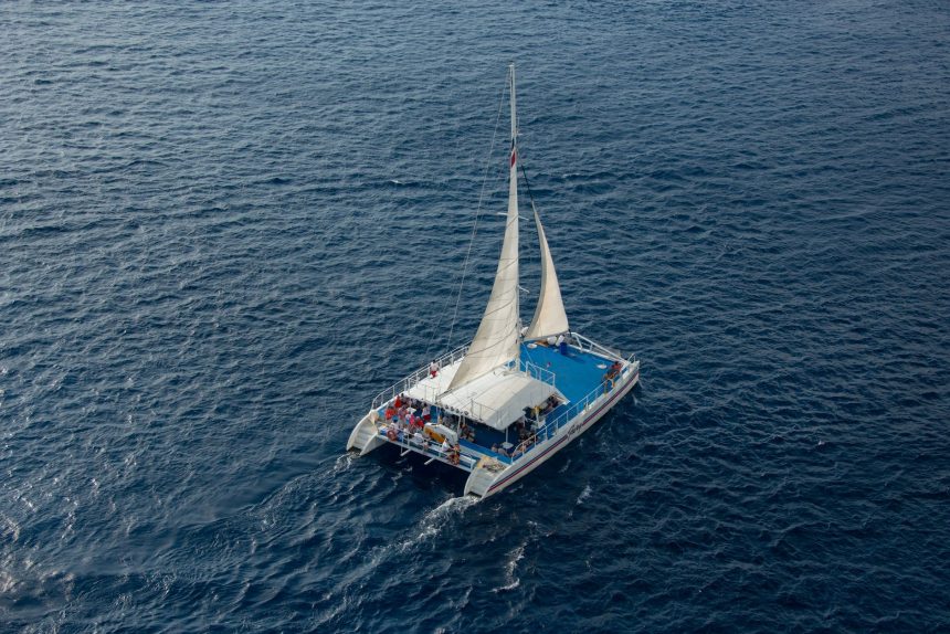 Vista aérea de um catamarã navegando com passageiros em águas azuis