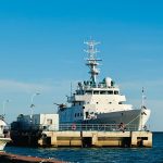 Grande embarcação branca de pesquisa atracada em um porto sob céu azul.