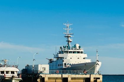 Grande embarcação branca de pesquisa atracada em um porto sob céu azul.