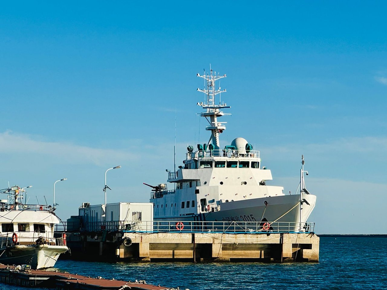 Grande embarcação branca de pesquisa atracada em um porto sob céu azul.