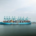 Grande navio porta-contêineres carregado atracado em um porto industrial.