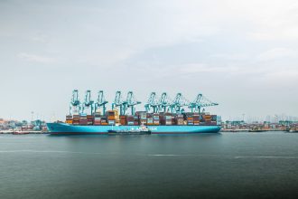 Grande navio porta-contêineres carregado atracado em um porto industrial.