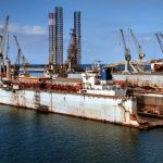 Estaleiro industrial com guindastes e embarcações atracadas em um porto.