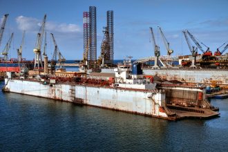 Estaleiro industrial com guindastes e embarcações atracadas em um porto.