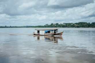 Embarcação tradicional de madeira navegando por um rio na Amazônia brasileira.